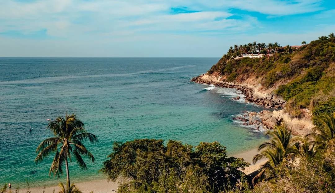 Cala de arena clara con palmeras y casas sobre el acantilado en Puerto Escondido