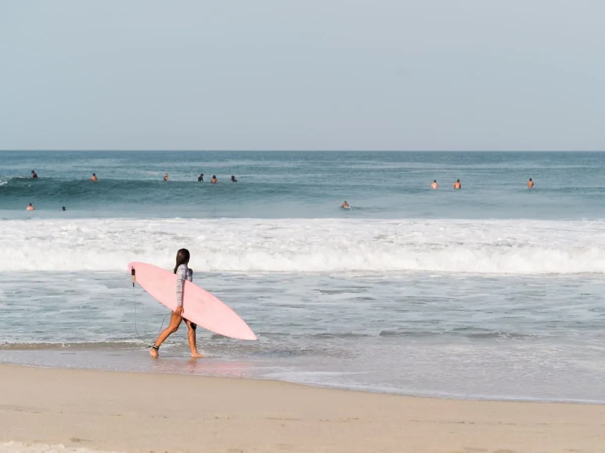 Surfista caminando por la orilla con su tabla mientras otros esperan olas