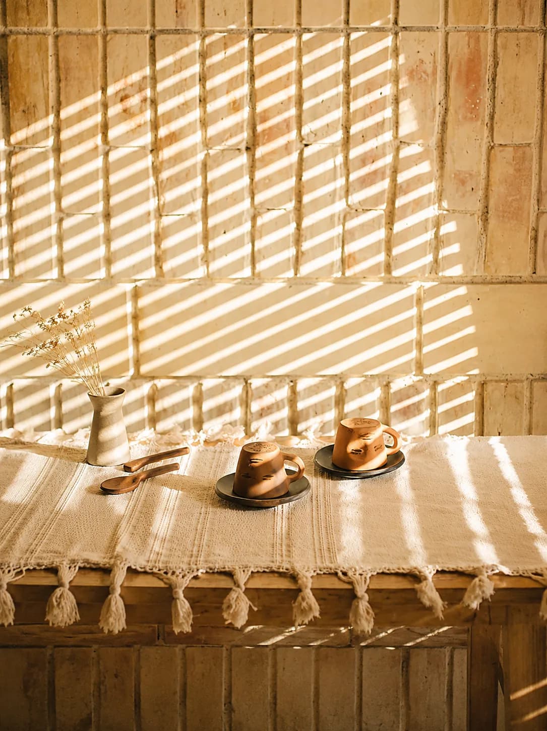 Mesa de café con tazas y pan dulce bajo la luz rayada de una celosía