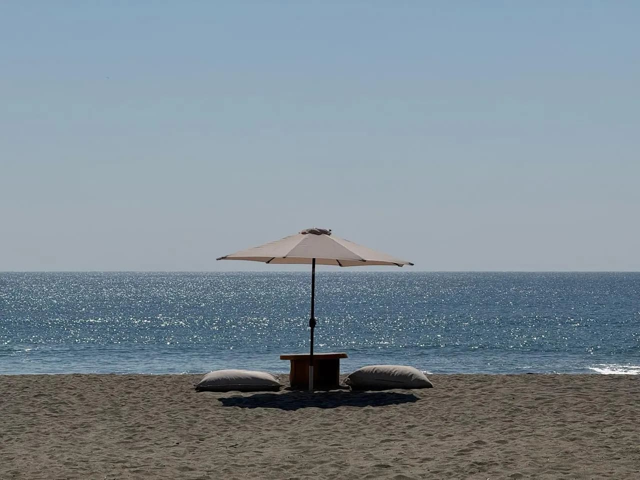 Sombrilla de playa y cojines sobre la arena oscura frente al mar