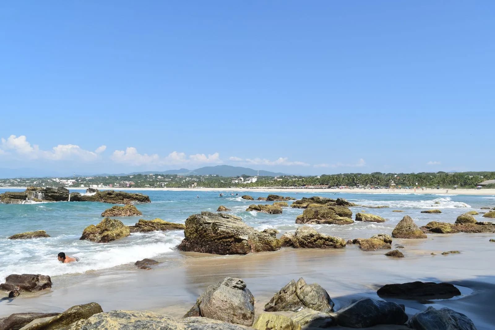Playa rocosa con oleaje y el pueblo de Puerto Escondido al fondo