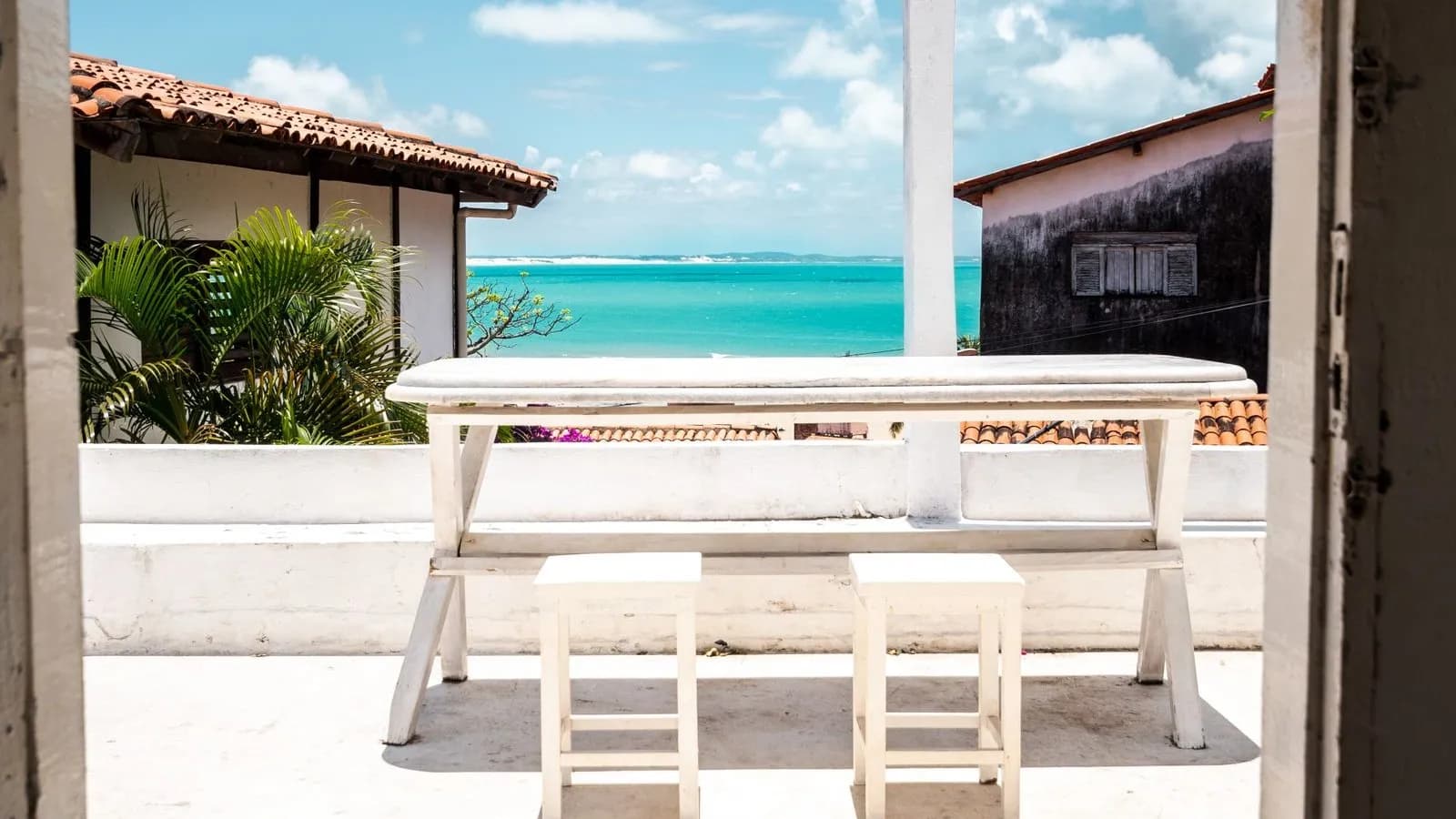 Terraza con mesa blanca y banquitos frente al mar turquesa