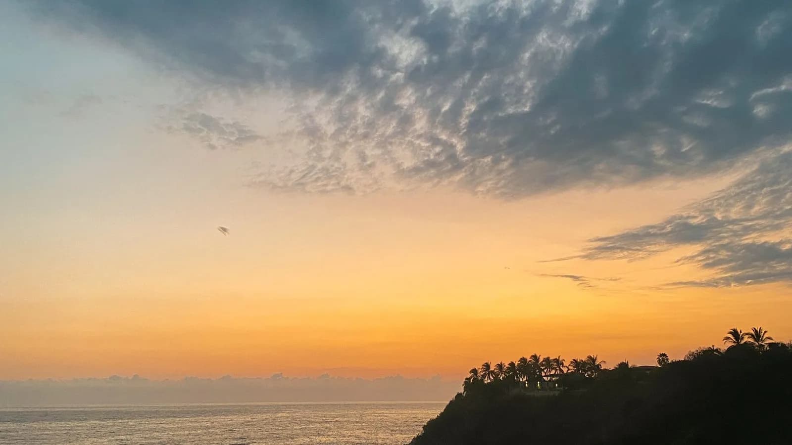 Atardecer sobre el mar con nubes encendidas visto desde una loma