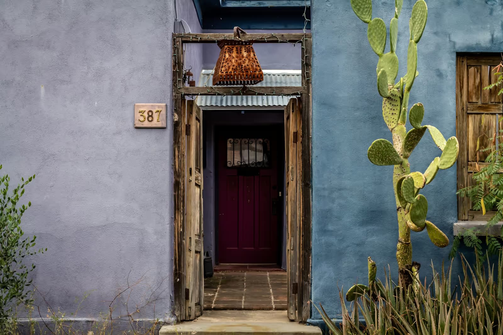 Entrada de una casa mexicana con puertas de madera y un nopal
