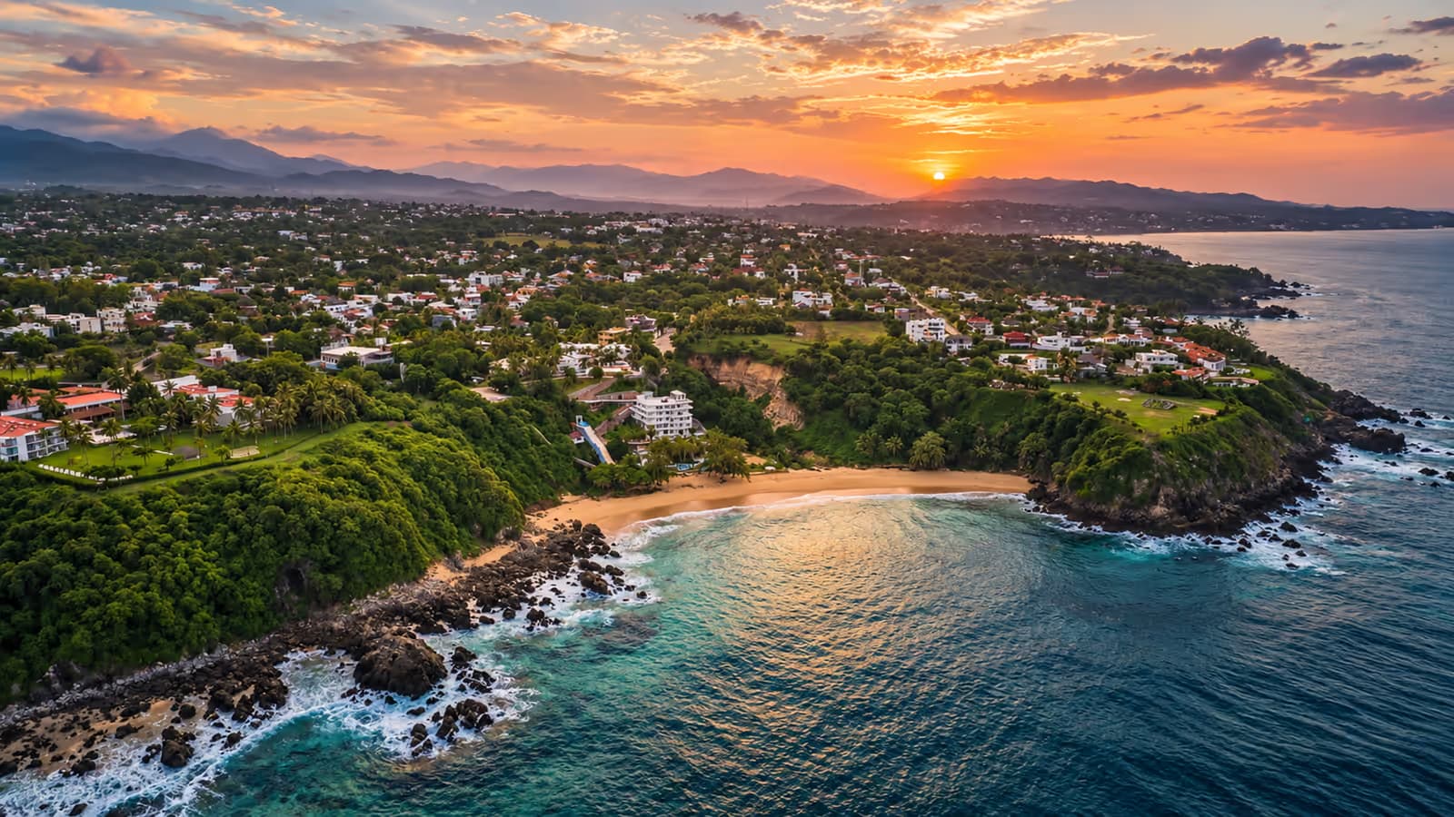 Vista aérea al atardecer de la costa, con casas entre vegetación y el sol sobre las montañas